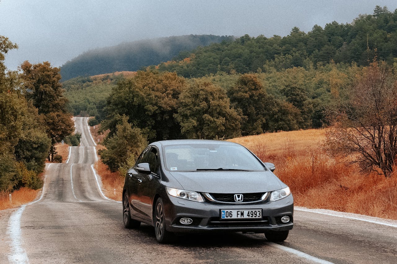 A car drives down a picturesque road surrounded by autumn foliage and rolling hills.